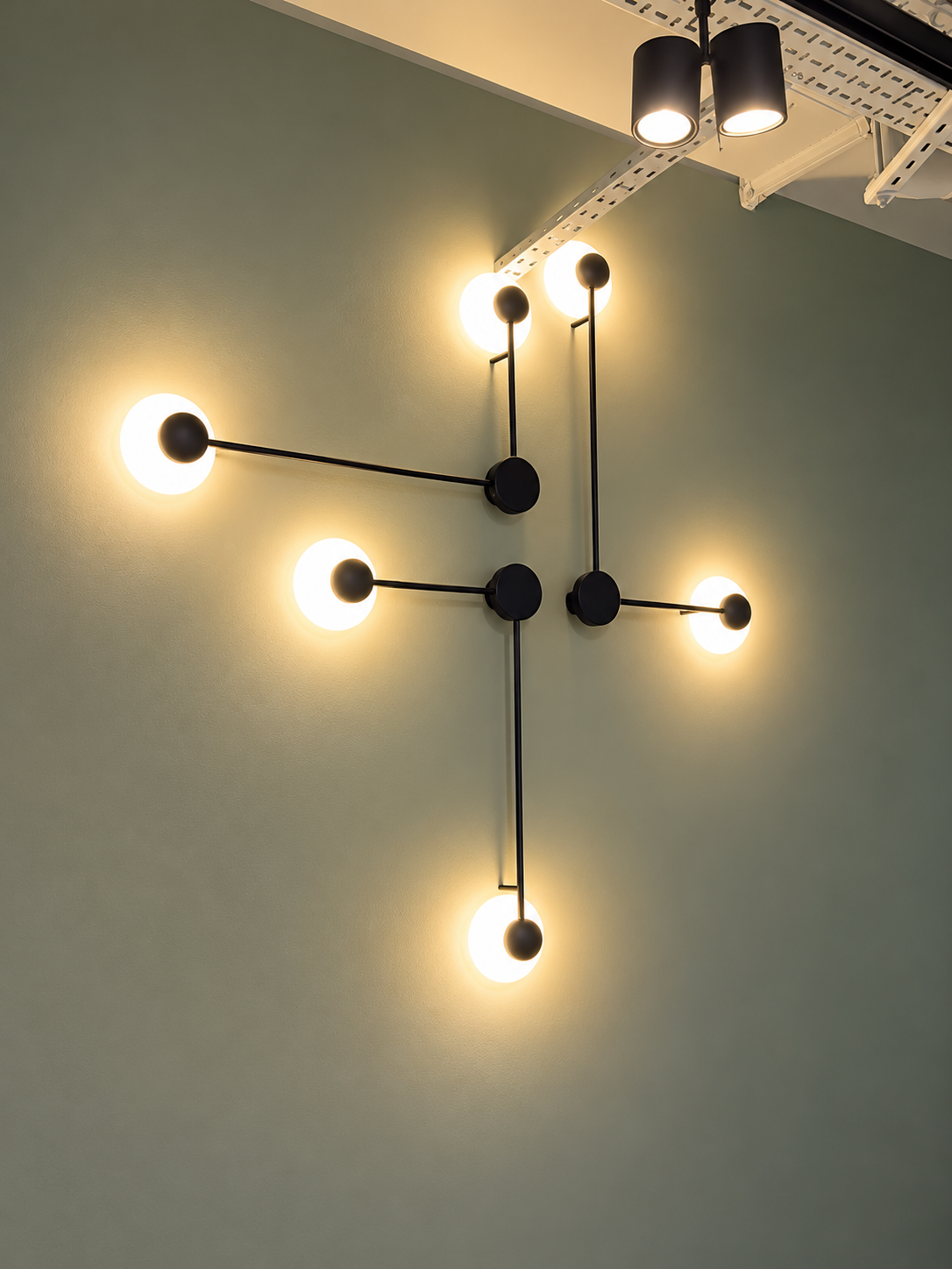 Black geometric wall lights with glowing spherical bulbs mounted on a pale green wall.