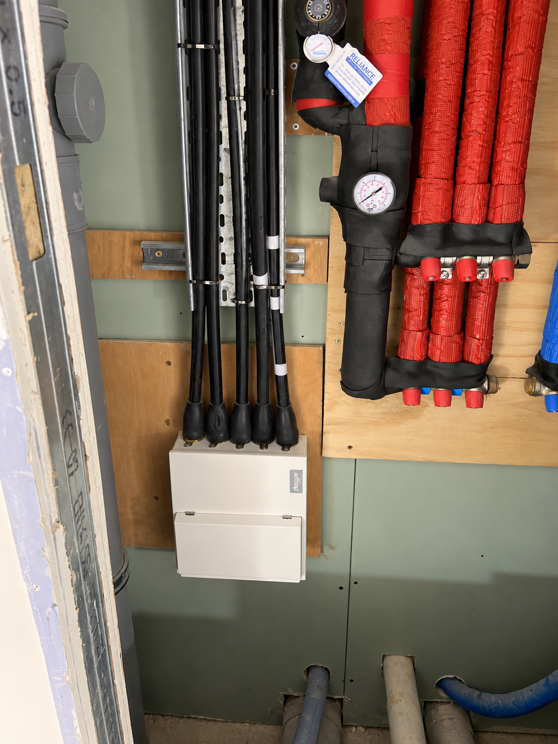 White electrical distribution box with thick black incoming cables beside insulated red and black pipework and pressure gauges.